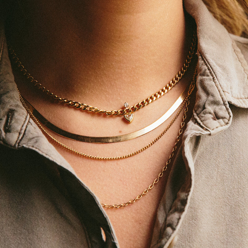 close up of a layered chain necklace, herringbone chain, and diamond curb chain necklace