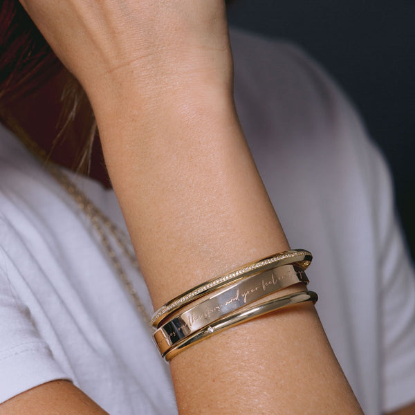 woman in white tshirt wearing Pave Diamond Line Knife Edge Cuff stacked with a Mantra Cuff bracelet