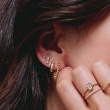 close up of woman's ear wearing Zoë Chicco 14k Gold Pavé Diamond Line Chubby Huggie Hoop Earring stacked with other diamond and gold earrings