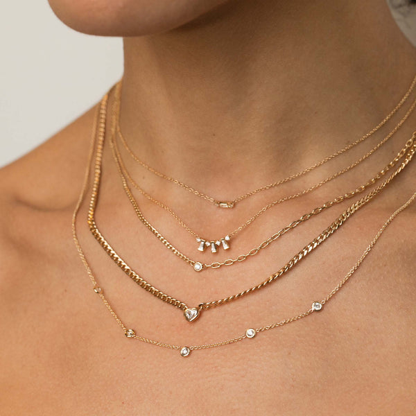 close up of a woman's neck wearing a Zoe Chicco 14k Gold Baguette & 2 Prong Diamond Necklace layered with a Tapered Baguette & Prong Diamond Necklace, Floating Diamond Mixed XS Curb Chain & Small Square Oval Chain Necklace. Floating Heart Shaped Diamond Small Curb Chain Necklace, and 5 Floating Diamond Station Necklace