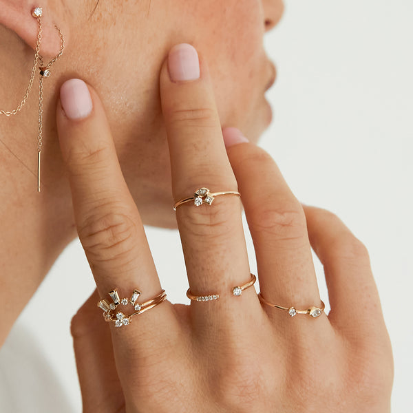 close up of woman resting her hand on her cheek wearing a Zoë Chicco 14k Gold Mixed Cut Diamond Cluster Ring and Pave & Prong Diamond Open Ring on her middle finger, a Prong Diamond Trio Ring and Tapered Baguette & Prong Diamond Curved Bar Ring on her index finger, and a Marquise and Prong Diamond Thin Band Ring on her ring finger