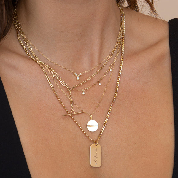 brunette woman in black tank top wearing Zoë Chicco 14k Gold Medium Pavé Diamond Line Disc Pendant Necklace layered with a balance Square Edge dog tag necklace, a Tapered Baguette Trio necklace, a Square oval link chain lariat toggle necklace, a Dangling Diamond Paperclip Chain Necklace