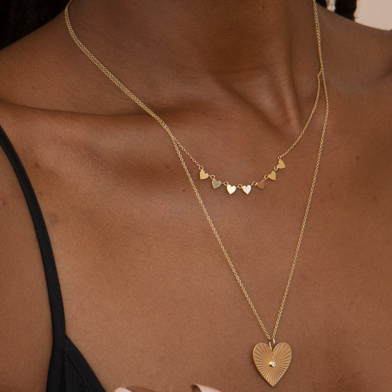 close up of woman in black top wearing a Zoë Chicco 14k Gold Medium Radiant Heart Diamond Bezel Medallion Pendant Necklace layered with a Pave Diamond 7 Itty Bitty Heart Necklace