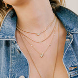 woman in a denim jacket wearing a Zoë Chicco 14k Gold One of a Kind 1.31 ctw Rose Cut Pear Diamond with Graduated Floating Diamond Stations Necklace layered with three other necklaces