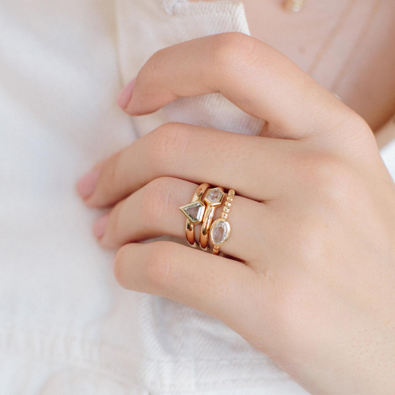 A woman wearing a Zoë Chicco 14k Gold Rose Cut Oval Diamond Beaded Band Ring layered with two other one of a kind diamond rings holding the collar of her white shirt