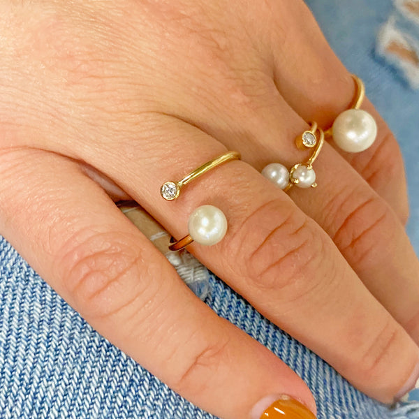 woman's hand wearing Zoe Chicco 14kt Gold Pearl and Diamond Bezel Bypass Wrap Ring with three other pearl rings on other fingers