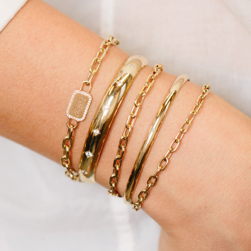 wrist wearing a stack of Zoe Chicco 14kt gold link chain bracelets and cuff bracelets
