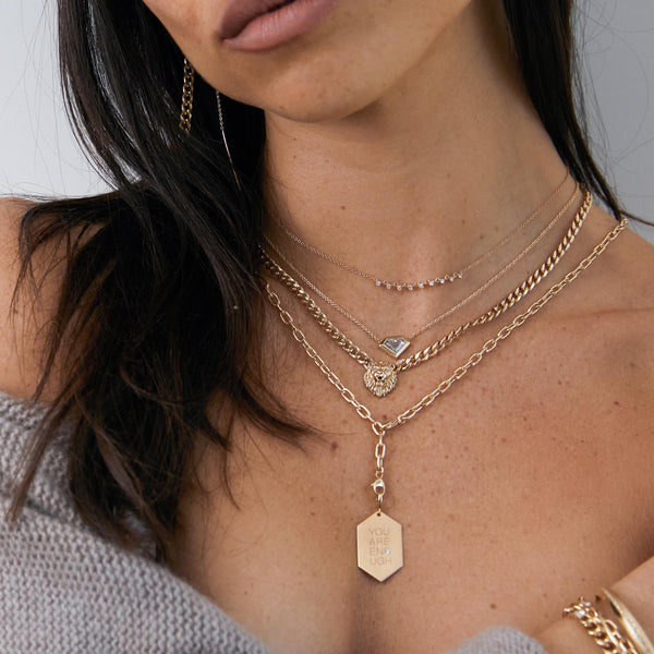woman with a grey sweater draped over her shoulders wearing a Zoë Chicco 14k Gold Medium "You are Enough" Hexagon Pendant on Adjustable Chain, Lion Head Curb Chain Necklace, One of a Kind Shield Diamond Bezel Necklace, and a 9 Linked Prong Diamond Necklace