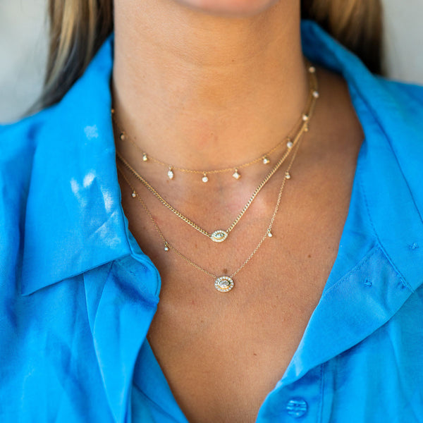 woman in blue top wearing Zoë Chicco 14kt Gold Oval Diamond Halo Necklace with Dangling Diamonds layered with two necklaces