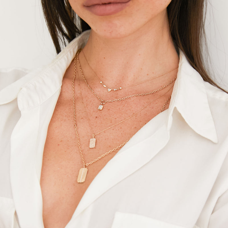woman in white shirt wearing a Zoë Chicco 14k Gold Small Square Oval Chain with Emerald Cut Diamond Necklace layered with a 5 Linked Mixed Cut Diamond Necklace, Full Pave Diamond Small Square Edge Dog Tag Necklace, and a Pave Diamond Line Medium Square Edge Dog Square Oval Chain Necklace