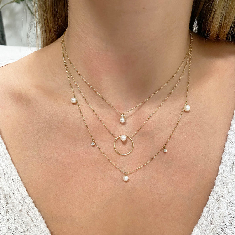 woman's neck wearing Zoë Chicco 14kt Gold Floating Pearl Medium Circle Necklace layered with two other pearl and diamond necklaces