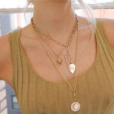 Woman in gold dress wearing a Zoë Chicco 14k Gold Pavé Diamond Initial Large Shield Charm Pendant with the letter N clipped onto a mixed paperclip chain necklace layered with 3 other chains