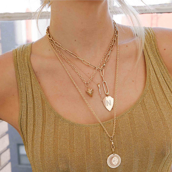 woman in a gold tank top dress wearing a Zoë Chicco 14k Gold Diamond Tennis Snake Drop Pendant Necklace layered with three other heavy chain necklaces
