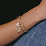 close up of woman's arm resting on her leg wearing  Zoë Chicco 14k Gold Medium Mantra Charm Rope Chain Bracelet