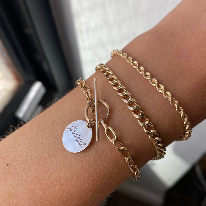 close up of a woman's wrist wearing Zoë Chicco 14k Gold Amore Charm Medium Square Oval Link Toggle Bracelet engraved with Grateful