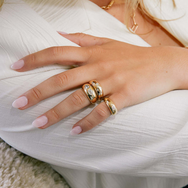 woman in white shirt resting her hand on her arm wearing a Zoë Chicco 14k Gold Scattered Star Set Diamonds Small Aura Ring and Flush Pear & Emerald Cut Diamond Medium Aura Ring stacked together  on her ring finger
