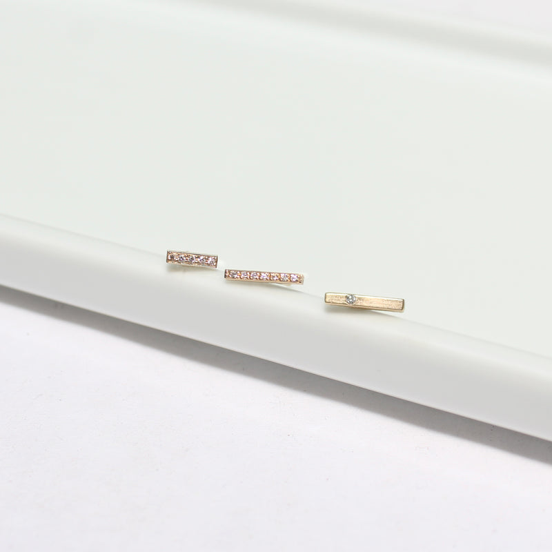 a Zoe Chicco 14k Gold Single Diamond Thin Bar Stud Earring laying with two pave diamond bar stud earrings in a row