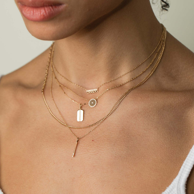 woman in white tank top wearing a Zoë Chicco 14k Gold Small Curb Chain & Pavé Diamond Bar Necklace layered with a Small Diamond Disc with Diamond Border Necklace, Small Pavé Diamond Line Square Edge Dog Tag Necklace, Mixed XS Curb & Small Square Oval Link Chain Necklace, and a Single Diamond Vertical Bar Pendant Necklace
