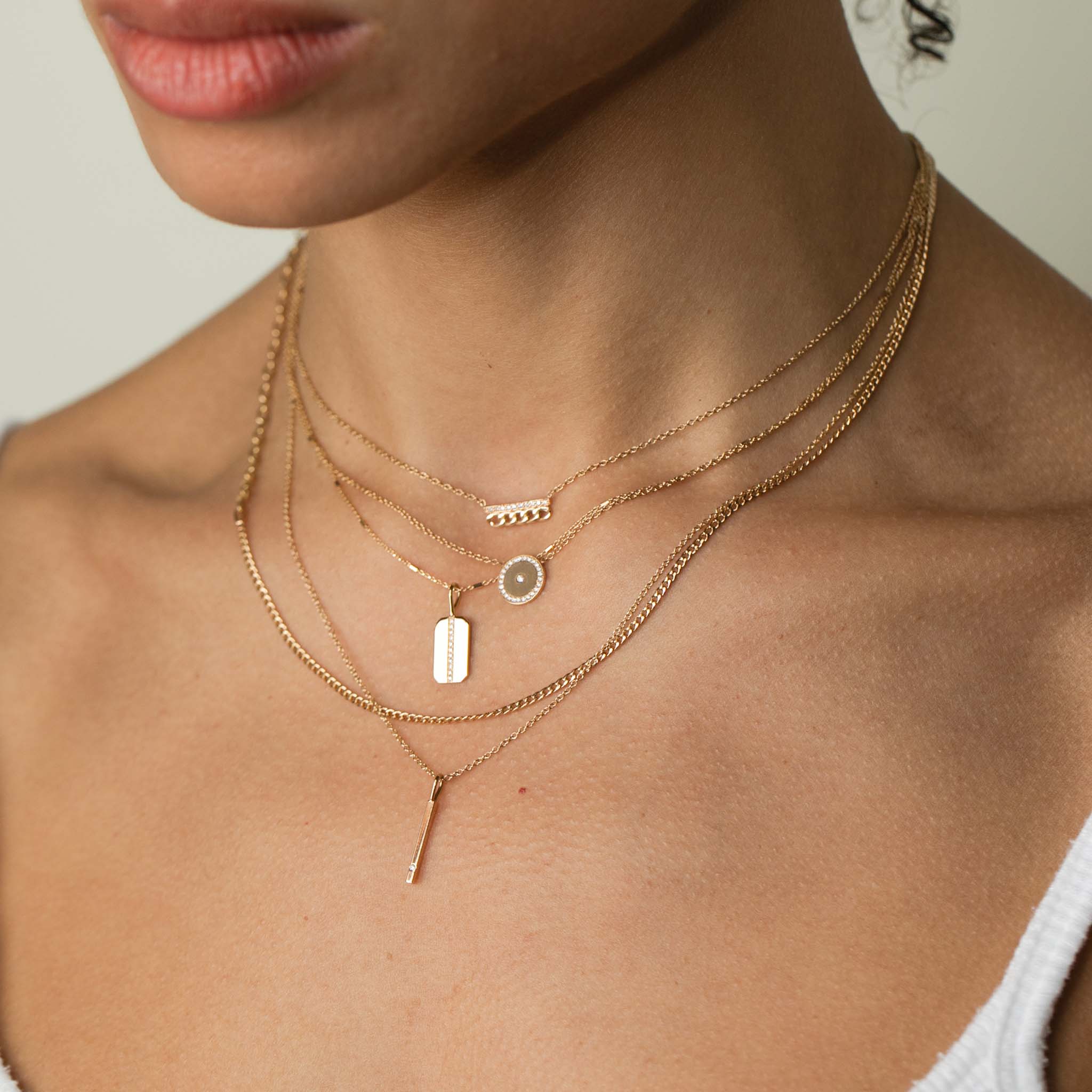 woman in white tank top wearing a Zoë Chicco 14k Gold Small Curb Chain & Pavé Diamond Bar Necklace layered with a Small Diamond Disc with Diamond Border Necklace, Small Pavé Diamond Line Square Edge Dog Tag Necklace, Mixed XS Curb & Small Square Oval Link Chain Necklace, and a Single Diamond Vertical Bar Pendant Necklace