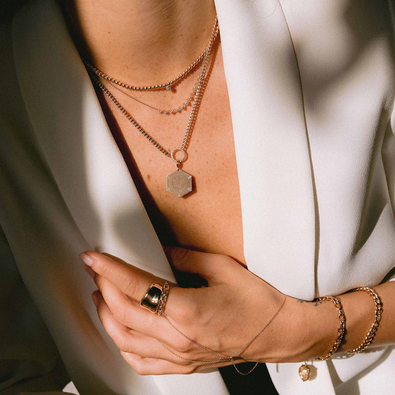 woman in white blazer wearing a Zoë Chicco 14k Gold Animal with Diamond Rays Hexagon Medallion Charm Pendant dangling off a Small Pave Diamond Circle Curb Chain necklace