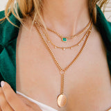 woman in green blazer wearing a Zoë Chicco 14k Gold Medium Curb Chain Emerald Cut Emerald Bezel Necklace layered with two heavy chain necklaces
