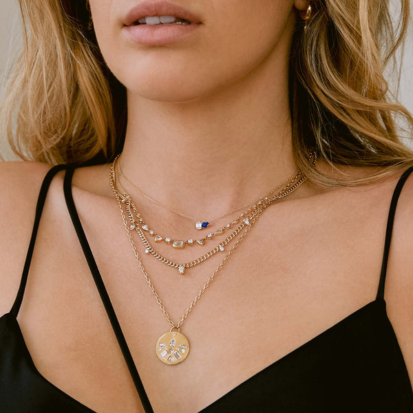 woman in black top wearing a Zoë Chicco 14k Gold Pear Blue Sapphire & Emerald Cut Diamond Necklace layered with three diamond necklaces