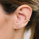 woman's ear with a diamond ear cuff, diamond stud, and a gold circle stud earring with a diamond and turquoise