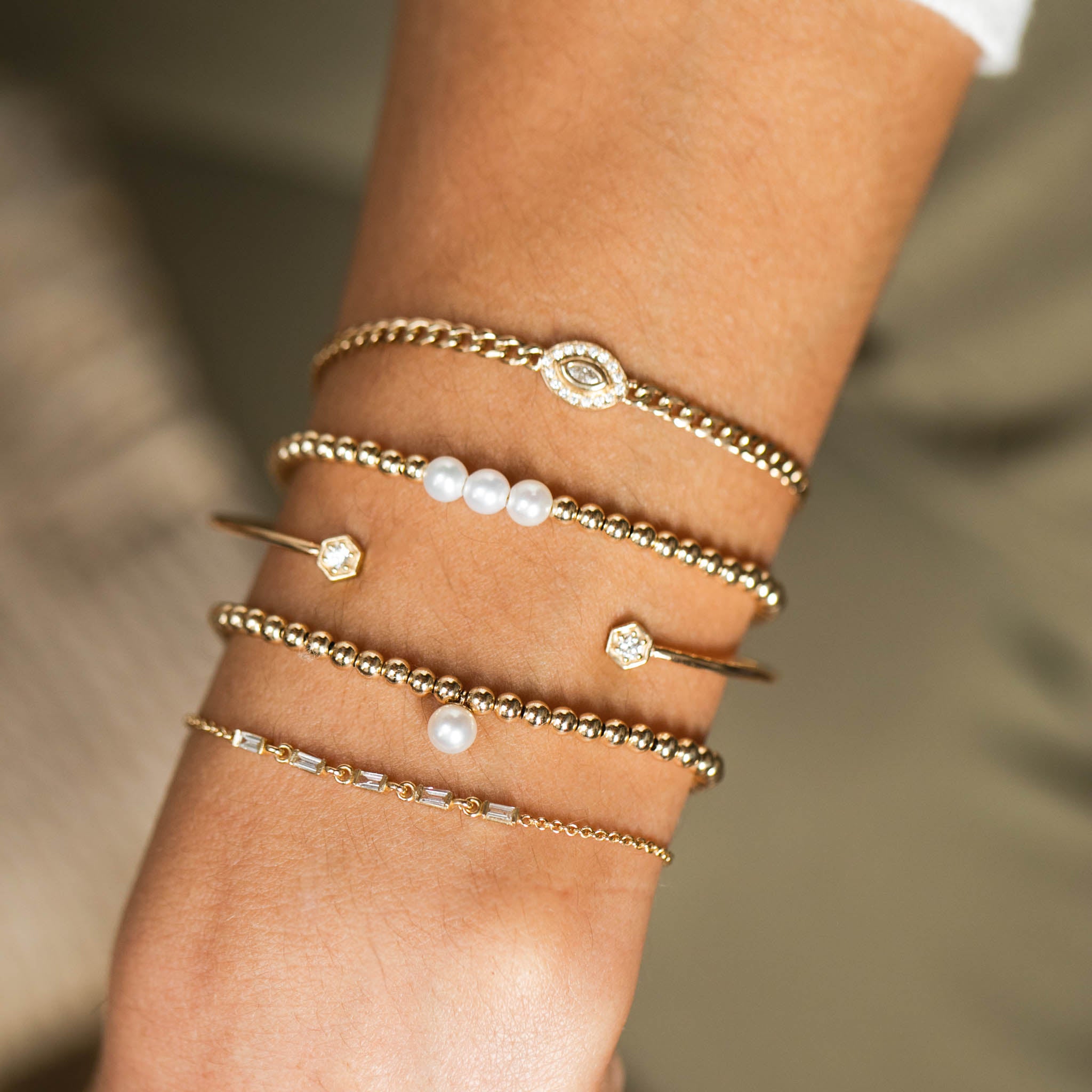 woman's wrist wearing Zoë Chicco 14k Small Curb Chain Marquise Diamond Halo Bracelet layered with pearl gold bead and diamond bracelets