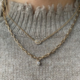 woman in sweater wearing Zoe Chicco 14k Extra Small Curb Chain Marquise Diamond Halo Necklace layered with a diamond bezel link chain necklace
