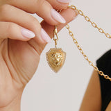 A woman holding up a square oval link chain necklace with a Zoë Chicco 14k Gold Lion Head Pavé Diamond Border Shield Pendant hanging from a fob clasp