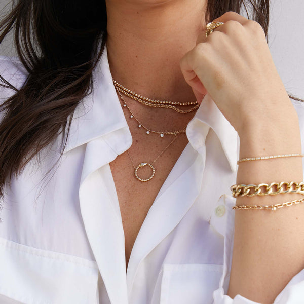 woman in white button up shirt wearing a Zoë Chicco 14k Yellow Gold Beaded Snake Circle with Star Set Diamond Necklace layered with other gold and diamond necklaces