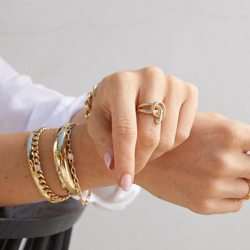 woman's hand wearing a Zoë Chicco 14k Gold Twisted Snake with Diamonds Ring with her arms crossed over a black chair