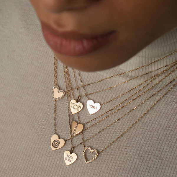woman in white turtleneck top wearing 3 Zoe Chicco 14k Gold Candy Heart Necklaces layered with a Zoë Chicco 14k Gold Pavé Diamond Line Heart Pendant Necklace, 14k Heart Padlock with Pavé Diamond Border Pendant Necklace, Diamond Bezel Heart Necklace, and a Pave Diamond Initial Heart Necklace