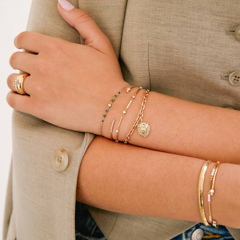 woman's wrist resting on her other arm wearing a Zoë Chicco 14k Gold Linked Graduated Blue Ombre Gemstone Bolo Bracelet layered with three other bracelets