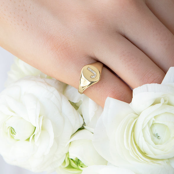 Zoë Chicco 14kt Gold Pave J Initial Signet Ring on a pinky finger with white roses in the background