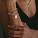 woman holding her arm up wearing a Zoë Chicco 14k Gold Small Sunbeam Charm Large Square Oval Link Bracelet on her wrist