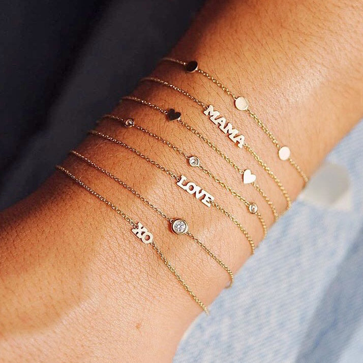 woman's wrist with Zoë Chicco 14kt Gold Itty Bitty XO Bracelet stacked with other Itty Bitty and diamond bracelets