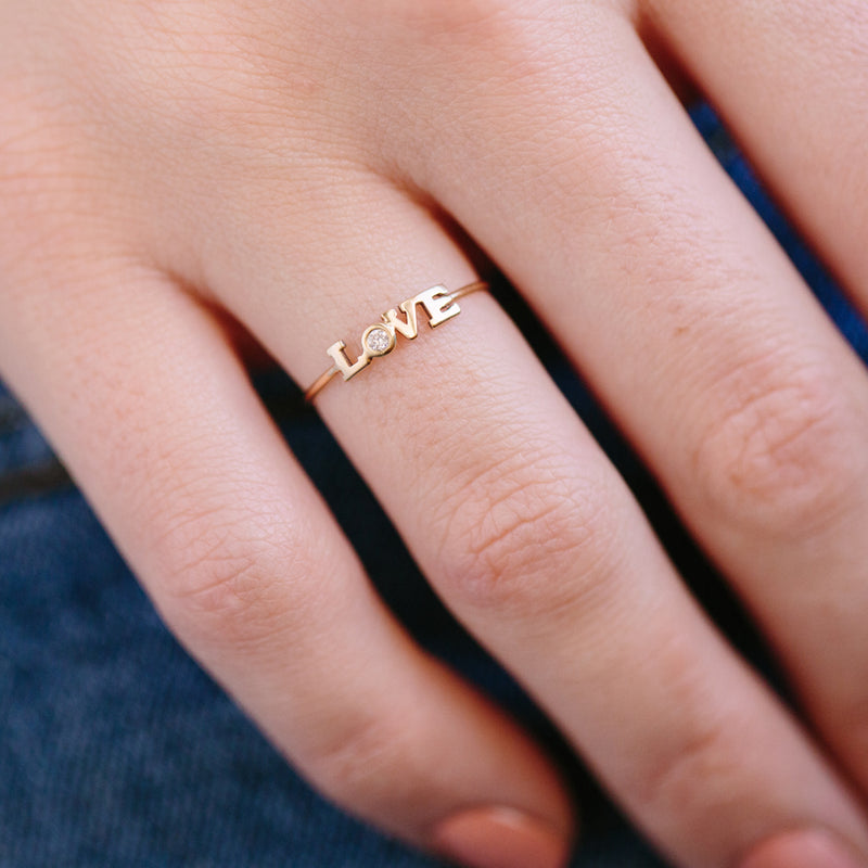 woman's hand wearing Zoë Chicco 14kt Gold Itty Bitty Diamond LOVE Ring on her ring finger