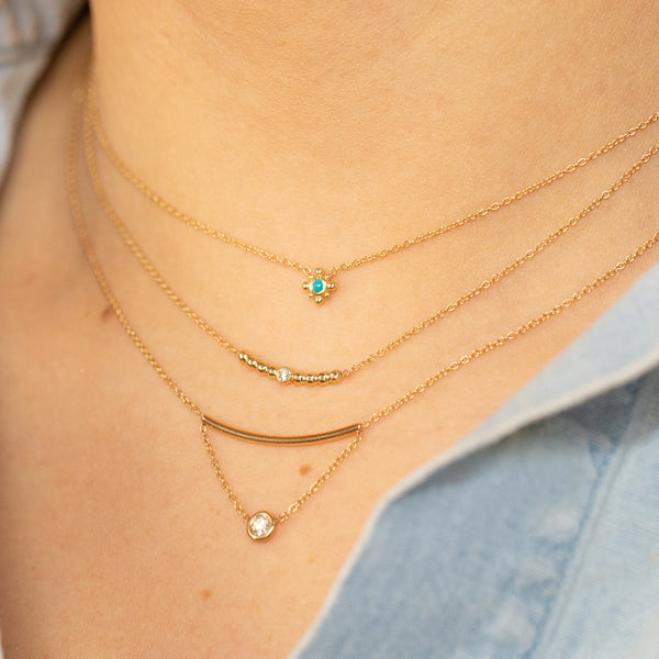 woman wearing Zoë Chicco 14kt Gold Tiny Bead Turquoise Starburst Necklace layered with two other gold chain necklaces