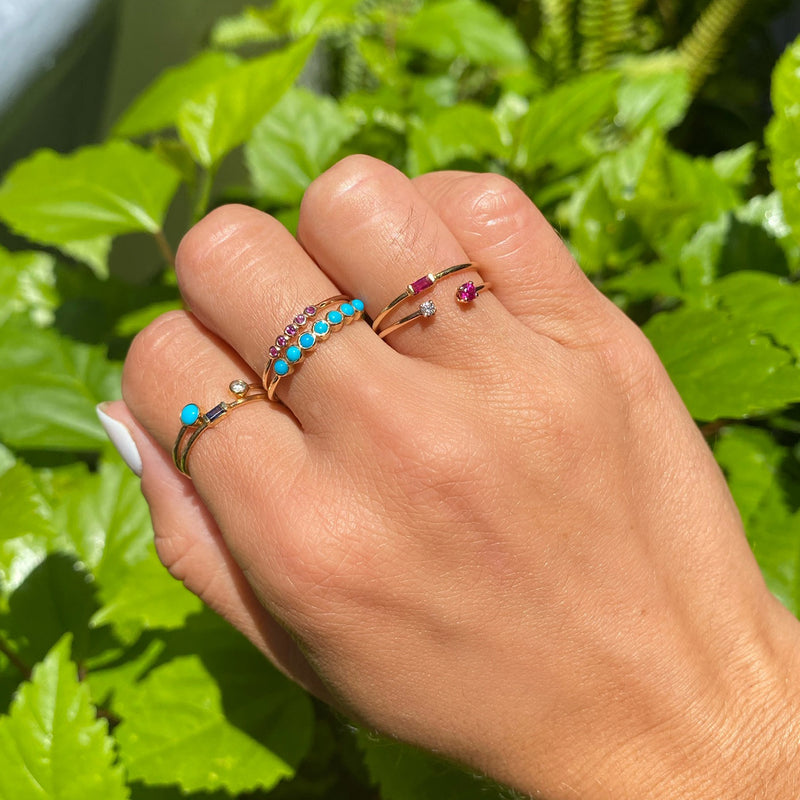 woman's hand wearing Zoe Chicco 14kt Gold Ruby Baguette Ring with other gemstone rings with a green plant in the background