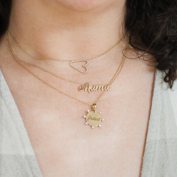 woman wearing a Zoë Chicco 14k Gold Sideways Pavé Diamond Heart Necklace layered with a Script Mama necklace and an amore necklace