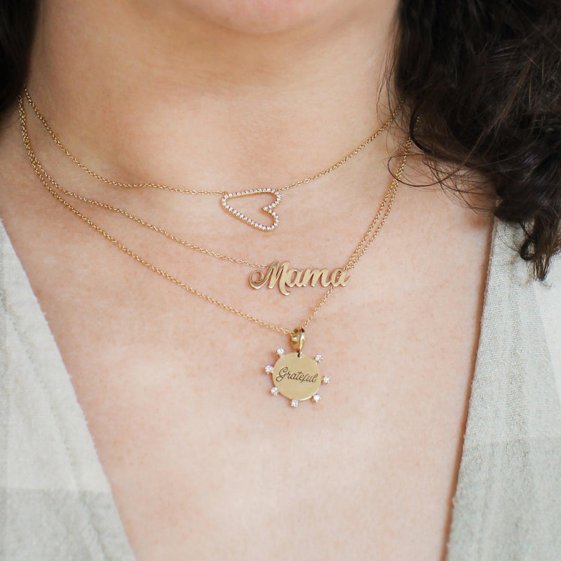 woman wearing a Zoë Chicco 14k Gold Script Letter Mama Necklace layered with a Pave Diamond Sideways Heart Necklace and an amore necklace