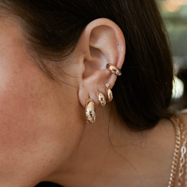 woman's ear wearing a Zoë Chicco 14k Yellow Gold Scattered Star Set Diamonds Medium Aura Hoop Earrings layered with other heavy metal earrings