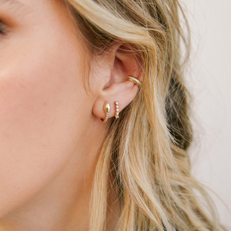 close up of woman's ear wearing a Single Zoë Chicco 14k Gold Pavé Diamond Snake Huggie Hoop Earring  layered with two other diamond earrings