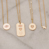 flat lay of Zoë Chicco 14kt Gold Pave Diamond Heart Disc Necklace with an elephant necklace, evil eye disc necklace, and an Eye Heart U dog tag charm necklace