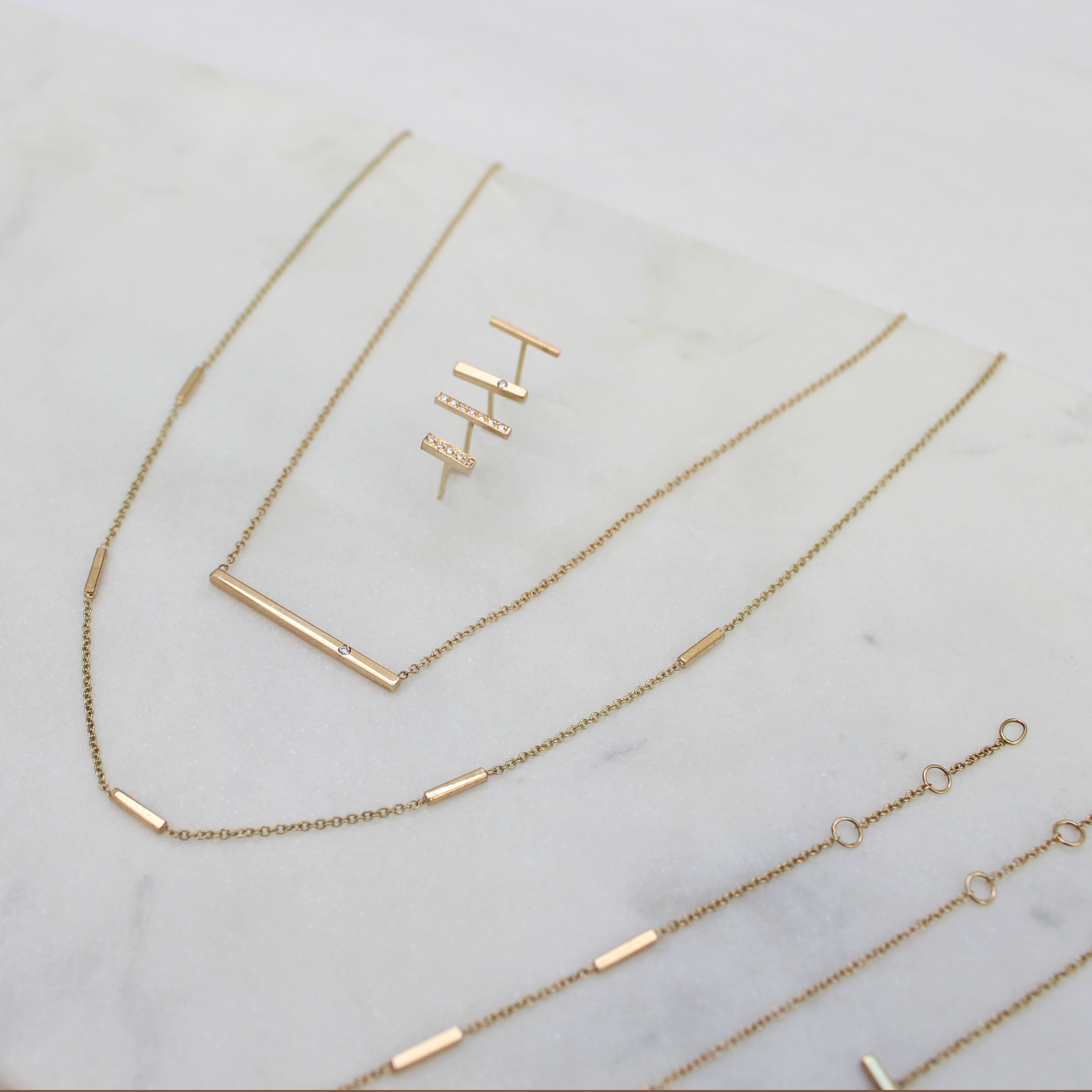 a Zoë Chicco 14k Gold Flush Set Diamond Bar Necklace laying flat on a marble top