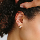 close up of woman's ear wearing a Zoë Chicco 14k Gold Emerald Cut Diamond Chubby Huggie Hoop Earrings layered with a Double Ear Cuff with Diamond Bezel