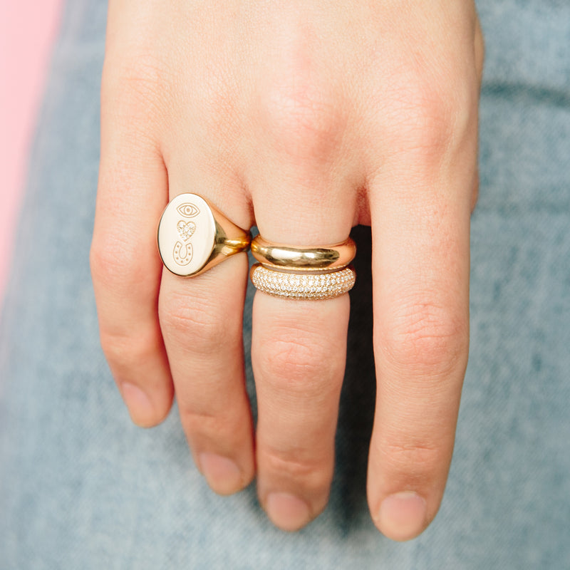 woman's hand wearing Zoë Chicco 14kt Gold Pave Diamond "Eye Heart U" Oval Signet Ring with two half round bands stacked together on another finger