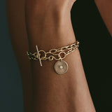 close up of woman's wrist wearing a Zoë Chicco 14k Gold XL Square Oval Link Pavé Diamond Toggle Bracelet layered with a sunbeam charm bracelet
