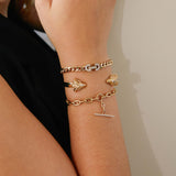 woman's wrist against a beige wall wearing a Zoë Chicco 14k Gold Vintage Pavé Diamond Horsebit Link Large Curb Chain Bracelet layered with a Rams Head Cuff and a Pave Diamond Toggle Bracelet